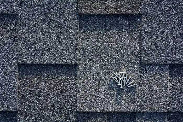 Close up view on asphalt roofing shingles and nails background.